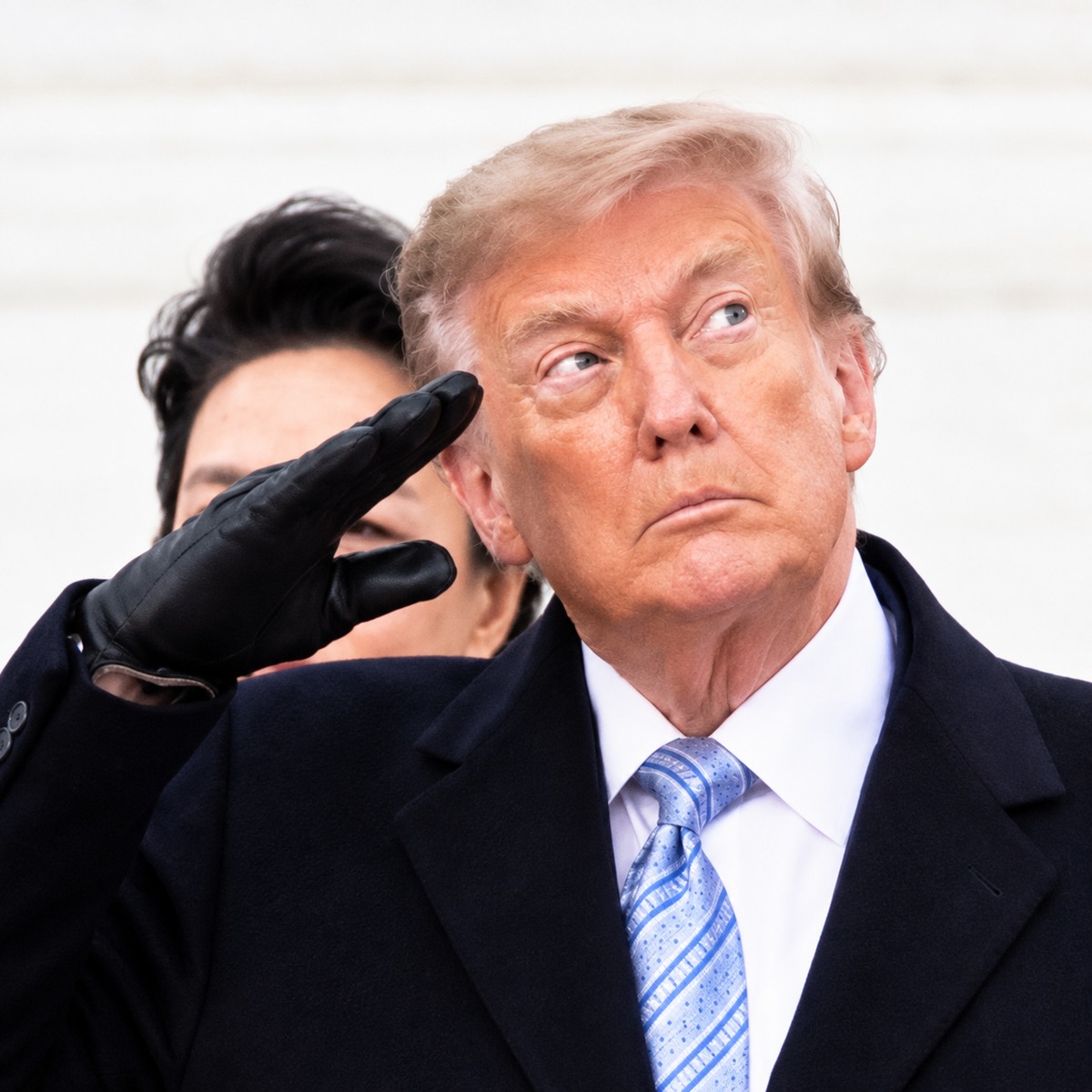 Donald Trump looking upward while a black-gloved hand is raised behind him